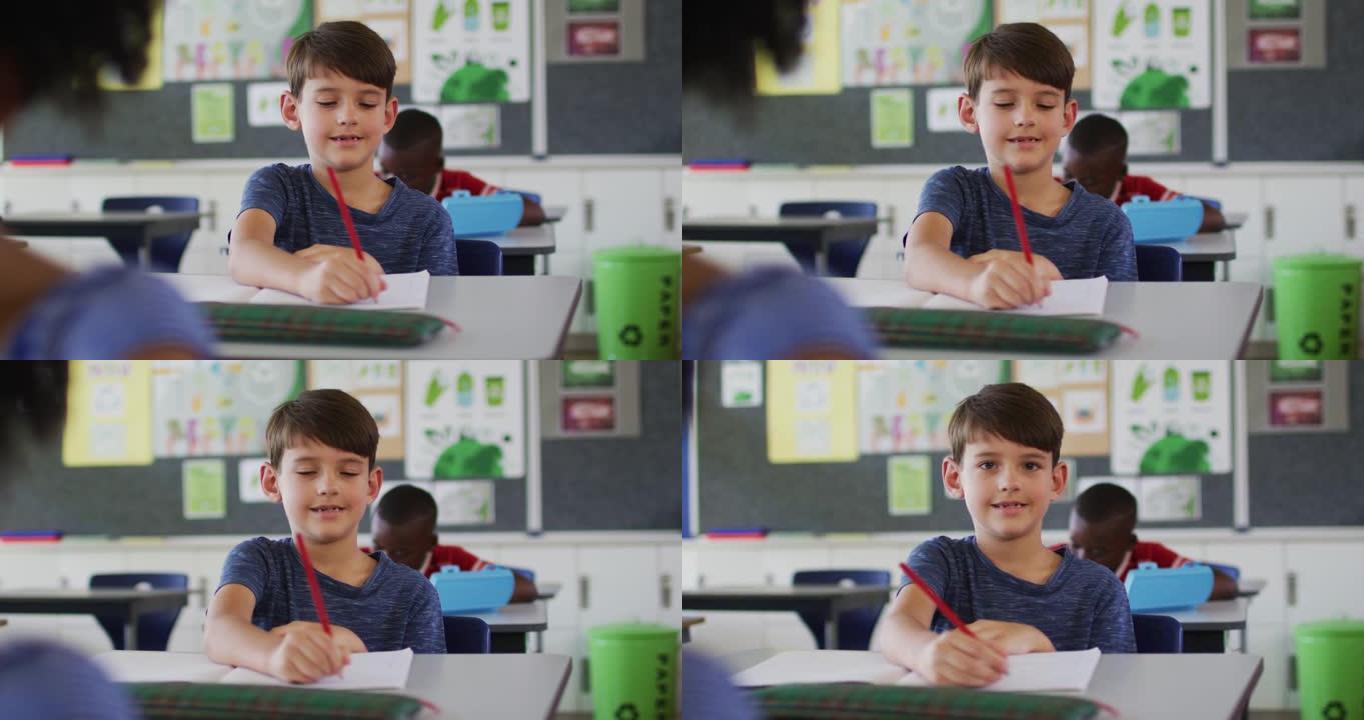 快乐的高加索男生的肖像坐在教室里，做笔记，看着相机