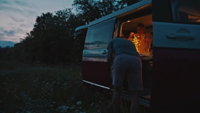 WS夫妇在黄昏时停在草地上的露营车内使用灯串