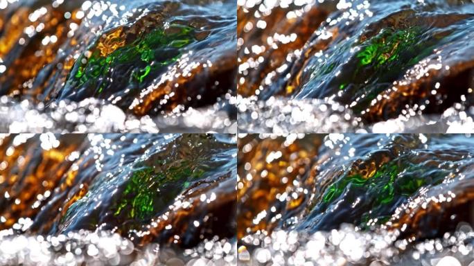超级SLO MO特写水从河中的棕色绿色大石头流下，水面上的阳光反射