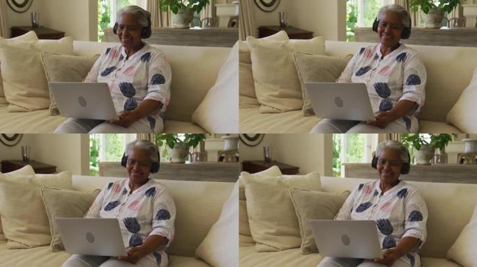 非裔美国高级妇女戴着耳机微笑，在家中通过笔记本电脑进行视频通话