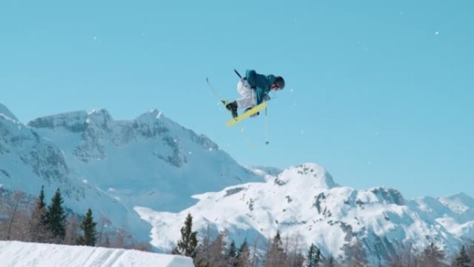慢动作: 男性自由式滑雪者在积雪覆盖的山顶上飞行