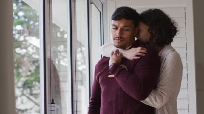 浪漫的西班牙裔夫妇拥抱站在窗户上的拥抱