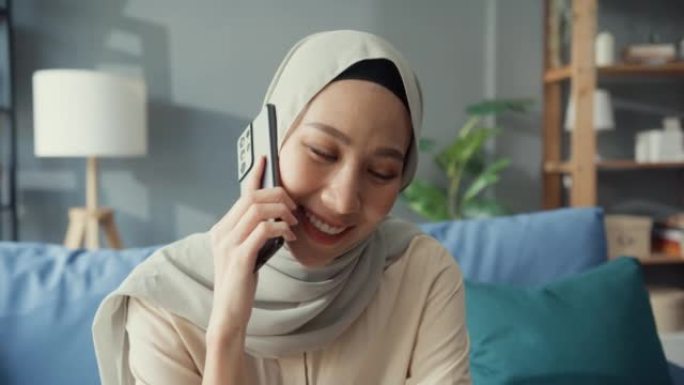 迷人的年轻亚洲穆斯林美女戴着头巾，在家里舒适的客厅与朋友和家人随意打电话。女孩伊斯兰社会距离检疫生活