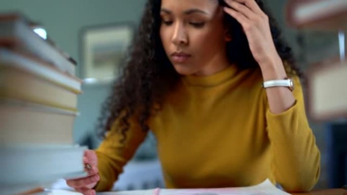 年轻压力重重的女人在家里的桌子上做作业。专注的女性在学习和做考试笔记时看起来不知所措。学生在努力实现