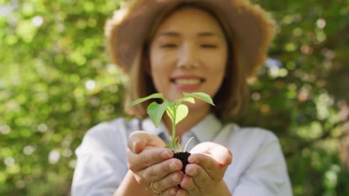 亚洲妇女在阳光明媚的日子里在花园里拿着植物微笑