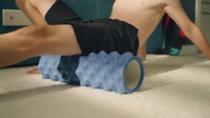 运动员男孩在地毯上使用泡沫滚筒在家里伸展肌肉热身
