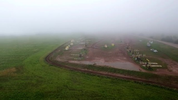 雨后雾天油田集群油泵的空中飞出视图。泥泞的地面水坑艰苦的工作条件。