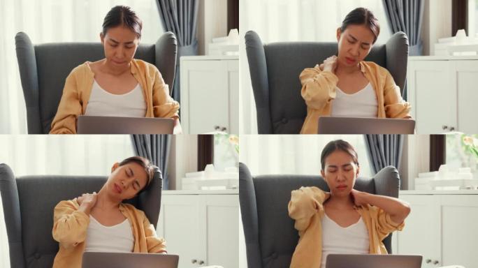 年轻的亚洲女女孩或大学生坐在沙发椅子上，用电脑笔记本电脑感到疼痛，在家里的客厅因加班而受伤。