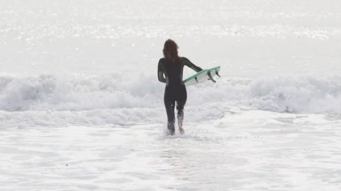 混血女子带着冲浪板跑进海里的后视图