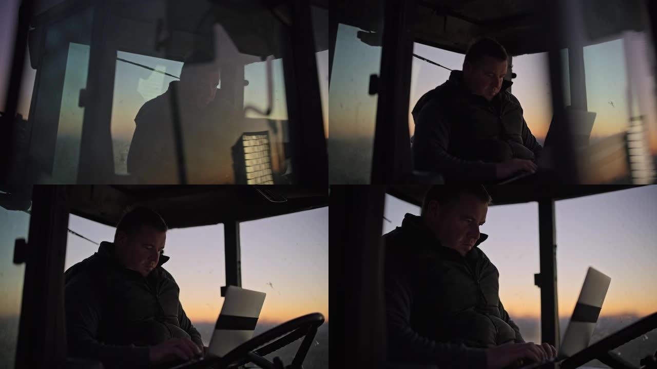 男性农民在日出时在拖拉机上的笔记本电脑上工作