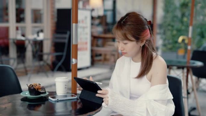 年轻的亚洲妇女在人行道咖啡馆使用平板电脑