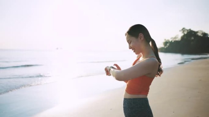 亚洲运动女性使用智能手表监控她在海滩上的跑步表现