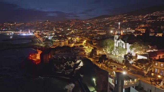 葡萄牙马德拉岛丰沙尔市夜景鸟瞰图。在傍晚的丰沙尔 (Funchal) 飞越海岸线，蓝色的日落天空