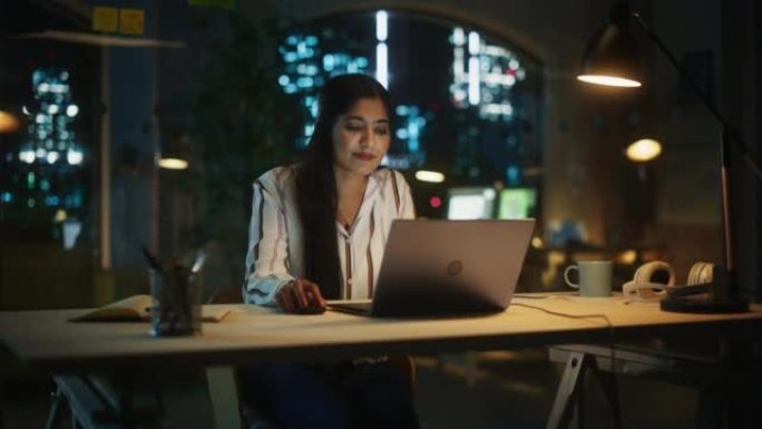 印度女性在创意机构工作，为客户实施现代商业战略。成功的专家晚上在办公室使用笔记本电脑。