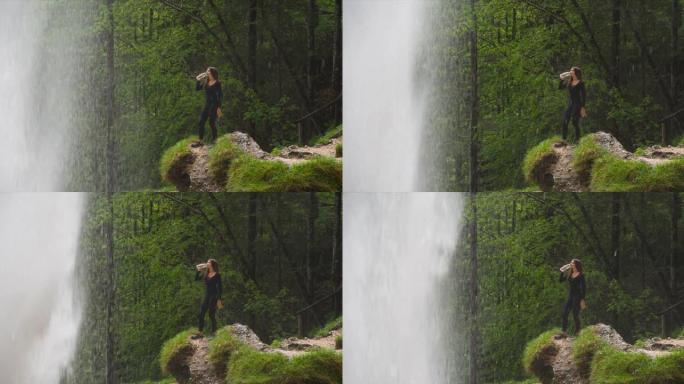 年轻女子在瀑布前喝水