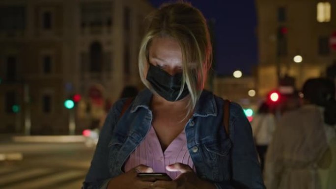 晚上在罗马的大街上使用智能手机戴着口罩的SLO MO女人