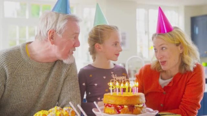 祖父母和孙女一起庆祝在家里的生日蛋糕上吹蜡烛