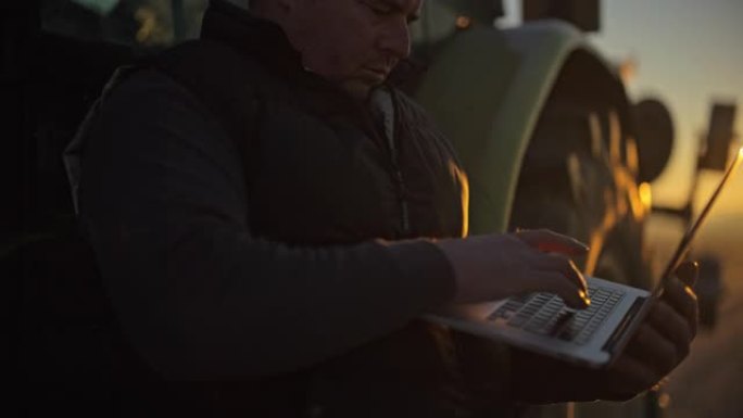 男性农民在日出时在农村地区使用笔记本电脑在拖拉机上工作