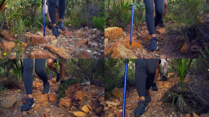 徒步旅行者用登山杖在山上的岩石小径上行走的特写镜头。一群积极冒险的朋友探索自然界崎岖的道路。在户外跋