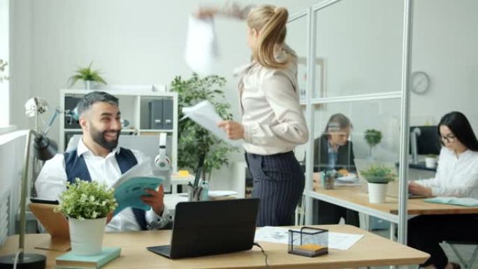 享受公司成功的多种族团队在办公室里扔纸跳舞拍手