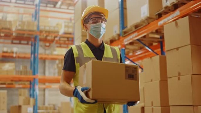 戴着医用口罩和安全帽的英俊男性工人的肖像背着纸板箱走过零售仓库，货架上摆满了货物。安全第一防护工作场