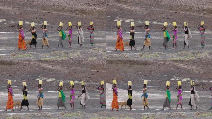 气候变化，干旱，水危机。侧视图。非洲妇女从肯尼亚图尔卡纳地区的火山泉水中收集塑料容器中的水后回家