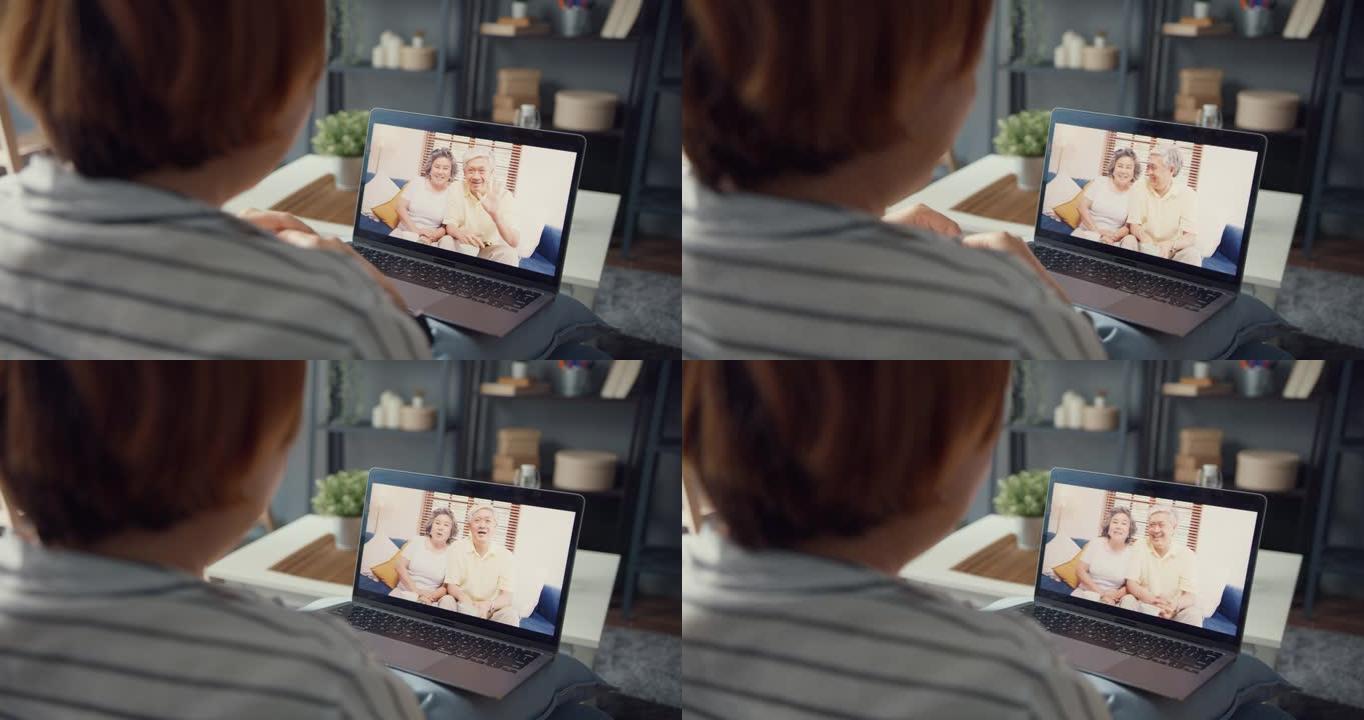 年轻的亚洲女孩使用笔记本电脑视频通话会议与年迈的家庭爸爸和妈妈聊天，在家工作时坐在客厅的沙发上。