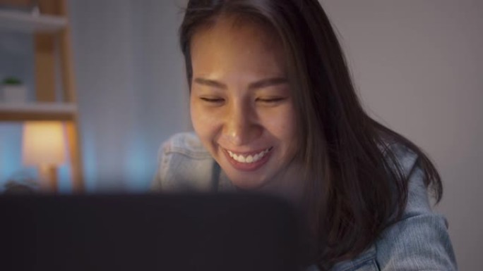 亚洲年轻女孩在家电脑工作到很晚快乐微笑成功。