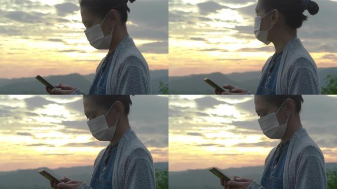 亚洲年轻女性戴着防护口罩，防止空气污染，并在日落背景下尝试通过智能手机找工作时冠状病毒Covid19