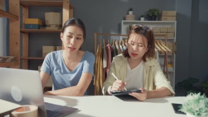 专业的两位亚洲女士，随意看笔记本电脑和平板电脑会议检查库存库存系统，准备订单并计划向客户运送产品。新