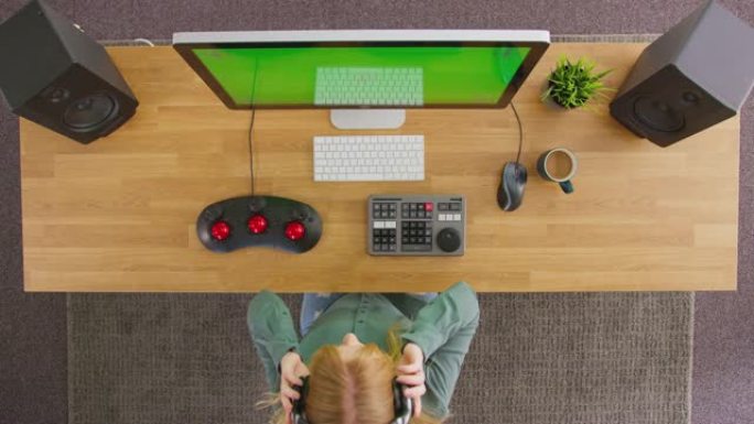 女性视频编辑器的俯视图戴上无线耳机，在创意办公室绿屏计算机上工作-慢动作拍摄