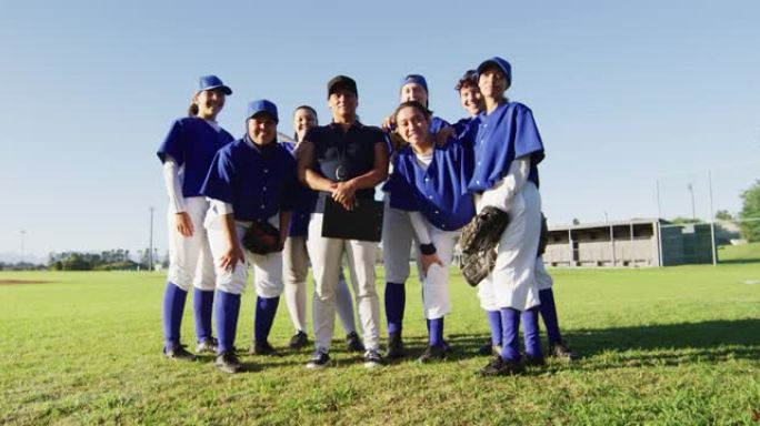 站在阳光明媚的球场上微笑着的女子棒球运动员和教练的多元化团队的合影