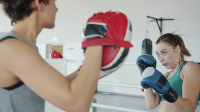 自信的女拳击手训练，伴侣戴着手套并使用现代设备进行拳击