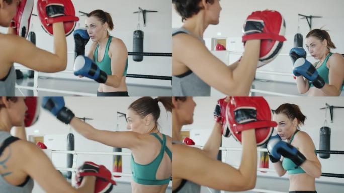 自信的女拳击手训练，伴侣戴着手套并使用现代设备进行拳击