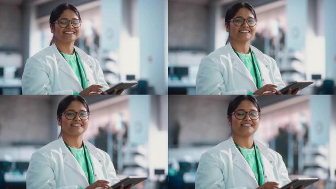 印度年轻女科学家的肖像使用数字平板电脑，看着相机，在实验室里微笑。自信的职业女性担任工程师，监控技术
