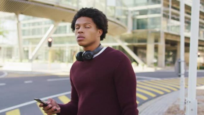 城市中的非裔美国人，在街上使用智能手机，戴着耳机和背包