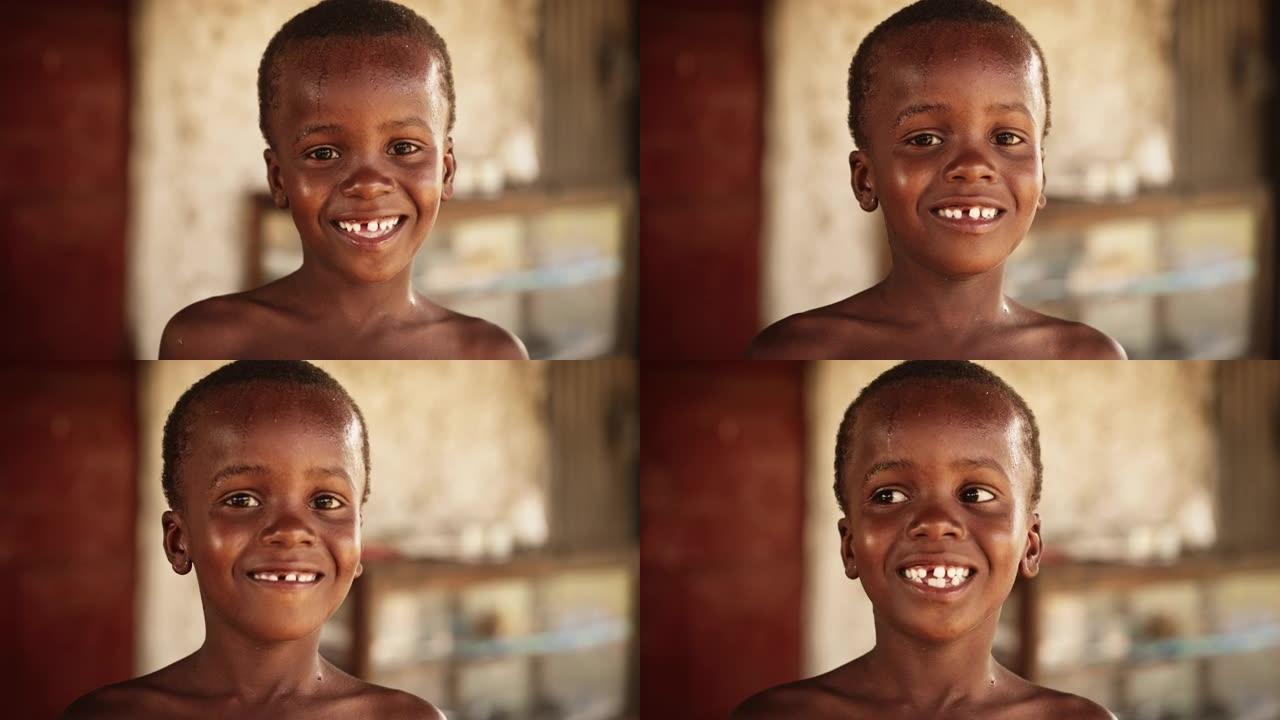 一个微笑的非洲孩子在农村地区笑着看着相机的肖像。在夏天炎热的天气里玩水玩得神清气爽后，小脸充满了快乐