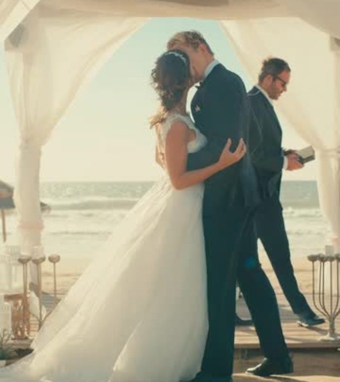 垂直屏幕: 美丽的新娘和新郎在海边的海滩上举行户外婚礼。浪漫夫妇和多民族文化最好的朋友的结婚场所。