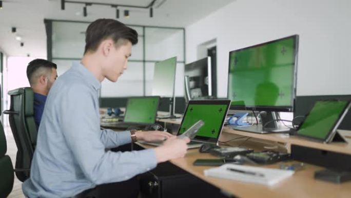 2名亚洲信息技术专业支持专业人员的侧视图，为信息技术解决方案使用多屏幕
