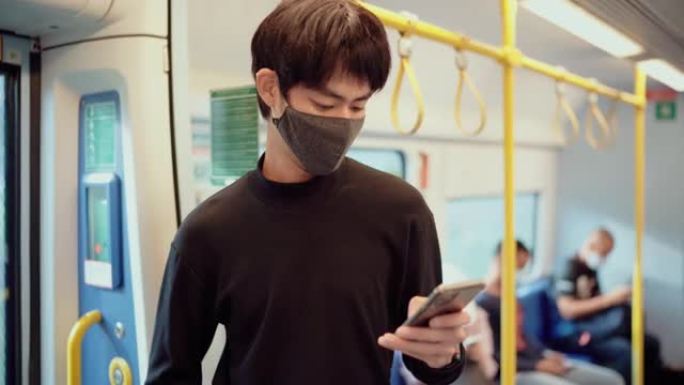 亚洲年轻男性在火车上使用智能手机并佩戴防护口罩