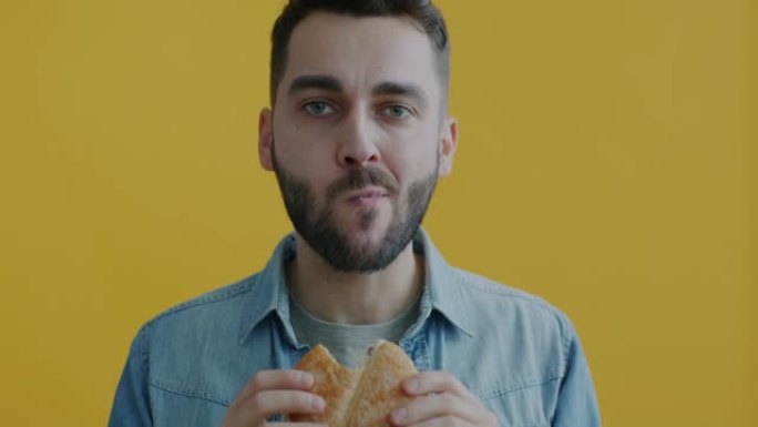 黄色背景下饥饿的年轻人吃汉堡咬咀嚼享受味道的慢动作肖像