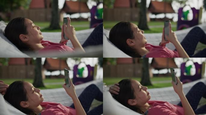 使用智能手机躺在吊床上的休息妇女