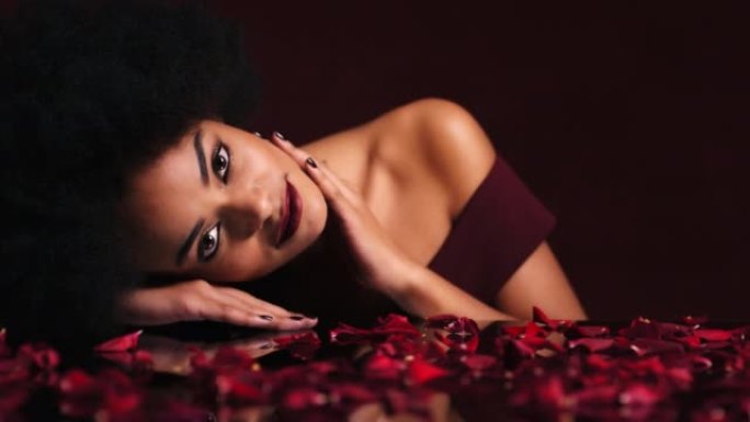 性感，诱人的黑人女人在玫瑰的花瓣中寻找爱情抚摸她的脸。美女，化妆和鲜花，来自巴西的性感女士。优雅，欲