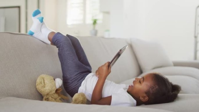 在家中使用数字平板电脑躺在沙发上的非洲裔美国快乐女孩