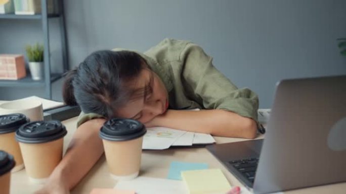 自由亚洲精疲力尽的女士努力工作，在办公室的木桌上睡了很多纸咖啡杯。