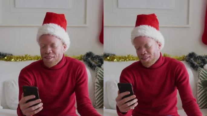 一名白化病男子戴着圣诞老人帽子进行视频通话，炫耀包裹的礼物的垂直镜头