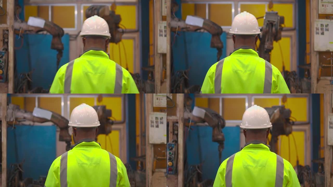 后视图，30岁的非裔美国人年轻人按下开关按钮编程机械臂，同时看工厂工业中的工作控制自动化机器人。工业