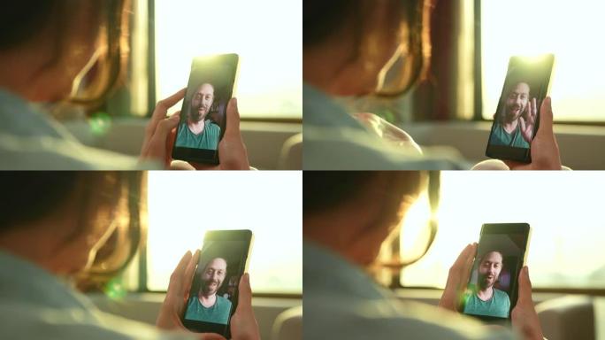 一个女人用手机和男朋友说话。在傍晚阳光照在她身上时拍摄。关注手机中的年轻人