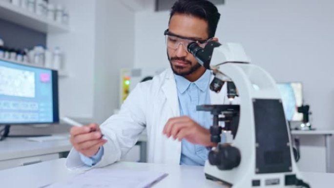 在医学研究实验室里，男性科学家使用显微镜观察血液样本，并在他的发现上写笔记。生物技术专家用手持摄像机