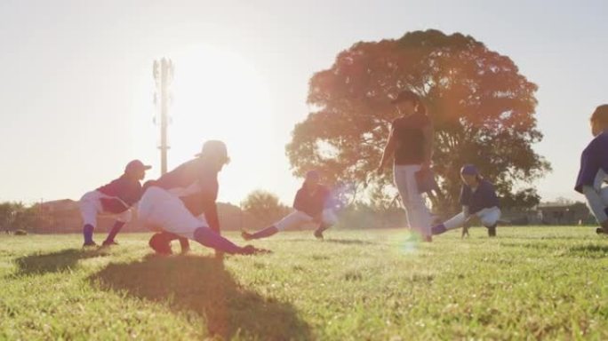 各种各样的女棒球运动员和教练在阳光明媚的球场上，蹲下和伸展双腿